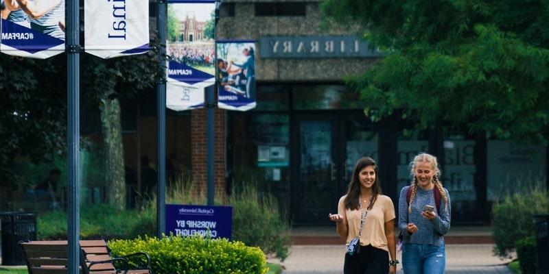 two college girls walking together down capital university path in front of library